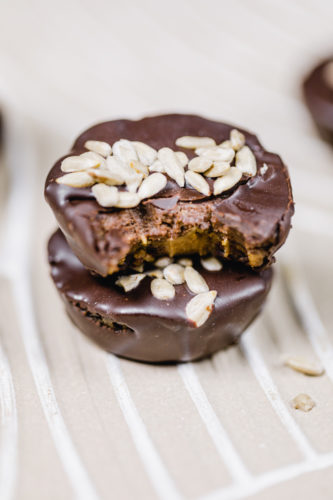 rohveganer snack in reese's form. bestehend aus zwei schichten: cashews und sonnenblumenkernmus. überzogen mit schokolade und mit sonnenblumenkernen dekoriert